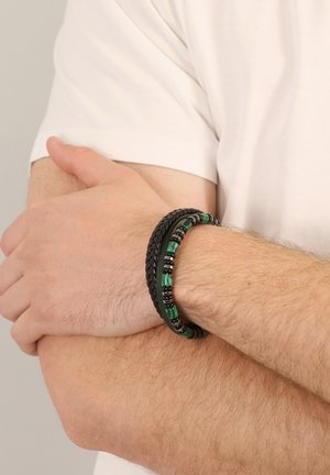 Verstellbares Mehrstrang-Armband aus geflochtenem schwarzem Leder und grün gestreiften Perlen mit schwarzen Metallakzenten am Handgelenk.