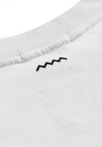 Biała bawełniana odzież z ribbowanym dekoltem oraz czarnym haftem w zygzak na plecach. Miękka faktura z widocznymi szwami.