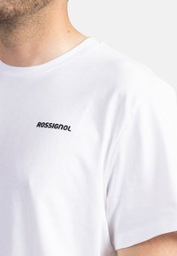 Bílý bavlněný tričko s kulatým výstřihem a krátkými rukávy, s malým černým logem "ROSSIGNOL" na levé hrudi.