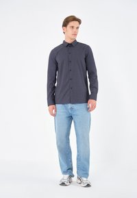 Chemise bleu marine à boutons avec un motif de petits points blancs, associée à un jean bleu clair et des chaussures de sport grises. Comprend un col classique.