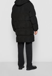 Sort dunjakke med hætte, der har et quiltet design og en afslappet pasform. Båret med mørke jeans og sorte sko.