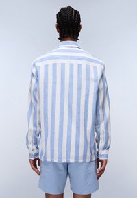 Camisa de lino ligera con rayas verticales en azul claro y blanco, con cuello clásico y puños abotonados, combinada con pantalones cortos azul claro.