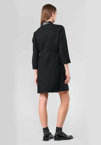 Vestido negro texturizado con mangas tres cuartos, cuello con solapa y corte recto, combinado con zapatos negros y calcetines grises.