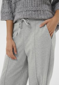 Hallid dressipüksid paelaga vöökohas, küljetaskutega ja pehme tekstuuriga viimistlusega. Taskus on nähtav käsi.