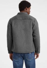 Giacca di lana grigia con colletto, due tasche laterali e polsini con bottone. Caratterizzata da un design pulito, una texture liscia e una silhouette dritta.