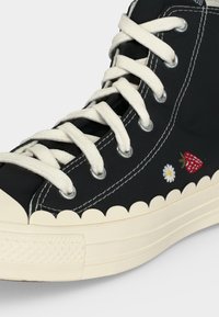 Μαύρο ψηλό αθλητικό παπούτσι με λευκά κορδόνια, κυματιστή εκρού σόλα, λευκά ραφές και μικρό κεντημένο φράουλα και μαργαρίτα στη πλευρά.