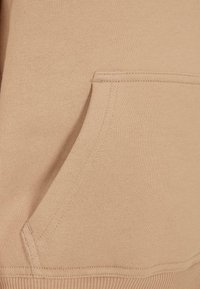 Tessuto di felpa beige con una consistenza morbida, caratterizzato da una tasca a marsupio e polsini e orlo a coste per una vestibilità aderente.