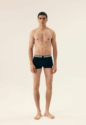 Schwarze Boxer-Shorts mit einem weißen Bund, der mit "HENDERSON" beschriftet ist, getragen von einem stehenden männlichen Modell mit nacktem Oberkörper. Glatte Stofftextur.