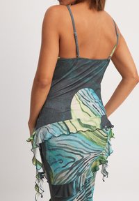 Sleeveless dress in dark fabric with a colorful circular and wavy pattern. Features ruffled accents along the hem and a fitted design.
