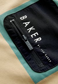 Crna tkanina torbice sa zatvaračima, sa natpisima "BAKER" i "by TED BAKER." Pozadina ima zelene i bež horizontalne pruge.