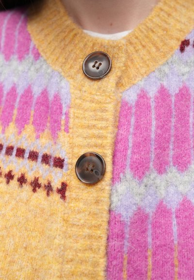 Vilnonis kardiganas geltonos, rožinės ir levandų spalvų, su gofruotu apykakliu, geometriniais raštais ir dviem dideliais rudais mygtukais priekyje.