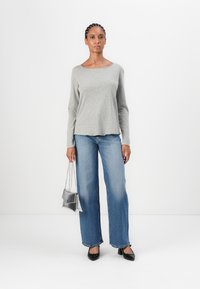 Grey long-sleeve top with a rounded neckline, paired with wide-leg blue jeans. The model holds a small silver handbag and wears black heels.