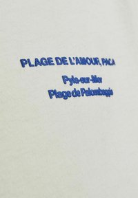 Balta medvilnė su mėlynu siuvinėjimu: "PLAGE DE L'AMOUR, PACA" ir "Pyla-sur-Mer Plage de Palombaggia."