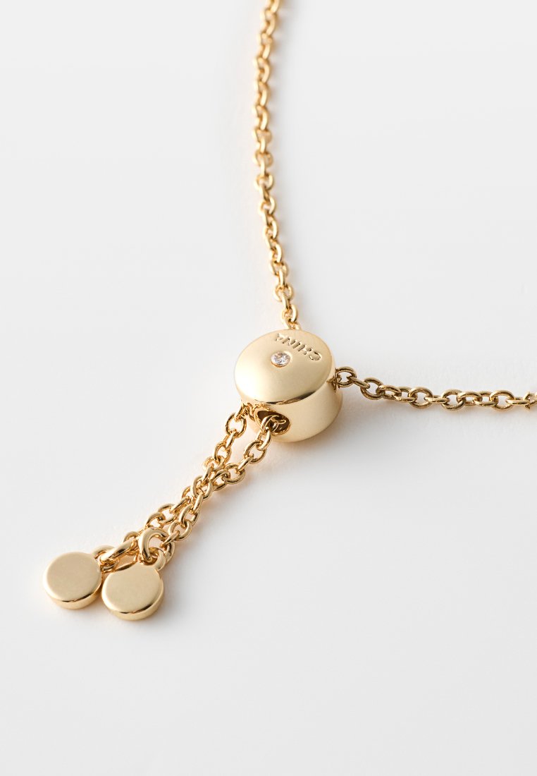 Goldfarbene Halskette mit einem runden Verschluss, der mit einem kleinen Diamantakzent versehen ist, verbunden durch eine feine Kette und abgeschlossen mit zwei runden Anhängern.