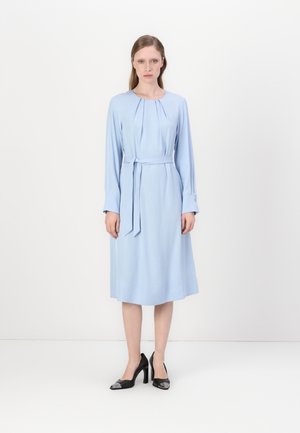 Vaaleansininen pitkähihainen mekko, jossa on pyöreä pääntie, laskokset ja samanlainen vyö. Yhdistetty mustiin korkokenkiin. Sulava kangas.