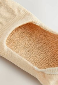 Ljusbeige ankelstrumpa med en texturerad, mjuk insida och slät yta, med en låg skärning för diskret användning.