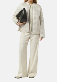 Helle, gesteppte Jacke mit hohem Kragen, kombiniert mit cremefarbenen weiten Hosen und einer schwarzen, kantigen Handtasche. Die Schuhe haben ein flaches Design.