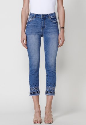 Blauwe denim jeans met een slim fit ontwerp, voorzien van decoratieve borduursels aan de zoom en rafelige randen. Middenhoog taille en klassieke vijf-pocket stijl.