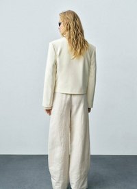 Ljust beige skräddarsydd jacka med strukturerade axlar, i kombination med vida krämfärgade byxor i texturerat tyg. Eleganta solglasögon fulländar looken.