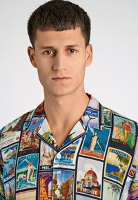Korte mouwen shirt met een kleurrijke print van vintage reisbestemmingen. Gemaakt van lichtgewicht stof, met een campkraag en knoopsluiting.