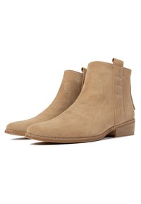Botines de ante beige con una textura suave, costuras decorativas, tacón ancho bajo y tiradores en la parte trasera para facilitar su uso.