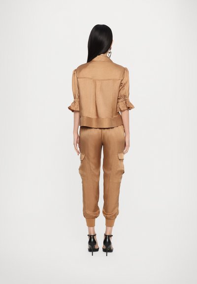 Braune Satin-Cropped-Jacke mit Puffärmeln, kombiniert mit passenden Cargo-Jogginghosen mit Seitentaschen und elastischen Bündchen. Schwarze Absatzschuhe.