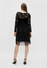 Svart spetsklänning med långa ärmar, genomskinlig kjoldel och detaljer med nyckelhål baktill. Tillverkad av ett lätt, texturerat tyg.