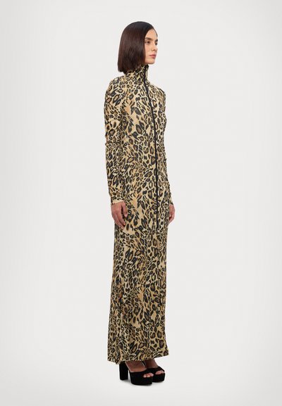 Long, form-fitting dress in a beige fabric with a black leopard print. Features a high collar and full-length sleeves, paired with black platform heels.