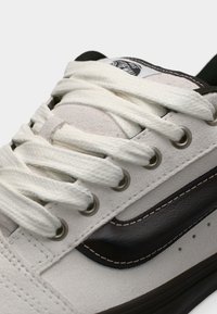 Άσπρο σουέτ αθλητικό παπούτσι με λείο καφέ δερμάτινο ρίγα, διαθέτει λευκά κορδόνια και μεταλλικά ρούμπελα. Διακριτικές τρύπες στην περιοχή των δακτύλων.