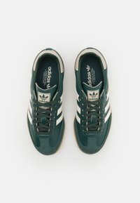 Tmavě zelené sportovní boty z kůže a látky, s bílými pruhy, béžovými doplňky a texturovanými gumovými podrážkami.