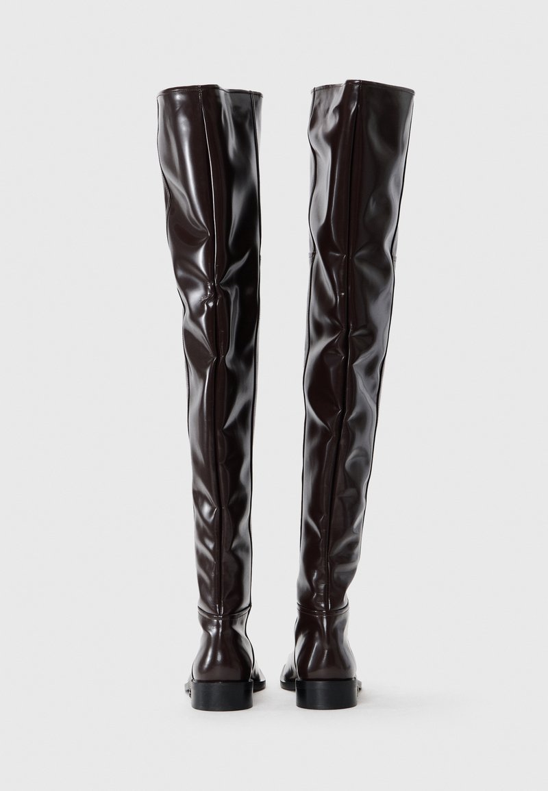 Bottes cuissardes marron en matériau brillant avec un design ajusté, présentant une texture lisse et des semelles plates à profil bas.
