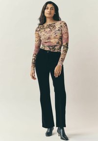 Langärmliges Oberteil mit floralem Design in Pink, Beige und Grün, kombiniert mit schwarzen Corduroy Schlaghosen und Absatz-Stiefeletten.