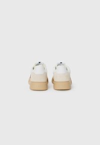Hvit og lys beige sneakers med såle i tannfarget gummi, semsket detaljer og et mønstret innersåle. Har merkevaren på hælen.