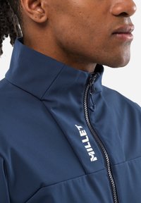 Navy blue softshell jacket with a high collar, front zipper, and white "Millet" logo on the chest. Smooth texture and fitted design.
