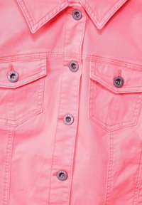 Bright pink denim jacket front with metal snap buttons and two chest pockets with flaps and visible stitching details.