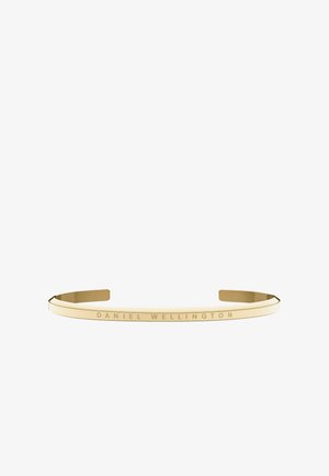Bracciale a manica in metallo color oro con una finitura liscia e lucidata, e dettaglio inciso "DANIEL WELLINGTON" lungo la banda.