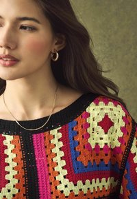 Hečkani džemper u višebojnim uzorcima s crnim rubom. Sadrži žive nijanse crvene, zelene i žute u raznim geometrijskim oblicima.