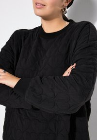 Zwarte gewatteerde sweatshirt met een textuurpatroon van harten, geribde neklijn en manchetten, met lange mouwen en een relaxte fit.