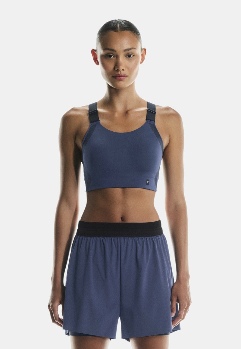 Marine sports-bh med brede stropper og rund halsudskæring, lavet af strækstof; parret med matchende marineblå shorts med en sort taljebånd.