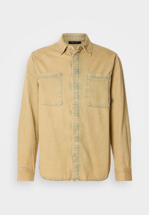 Lysegul denimskjorte med to brystlommer, knaplukning foran og krave. Stoffet har en subtil struktur og kontrastfarvede syninger.