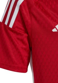 Jersey deportivo rojo hecho de tela texturizada, con franjas blancas en los hombros y un sutil patrón de diamantes en todo su diseño.
