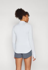 Hellblaues langärmliges Oberteil mit hohem Kragen, geribbelter Textur und flachen Nähten, kombiniert mit grauen Sportshorts. Rückansicht gezeigt.