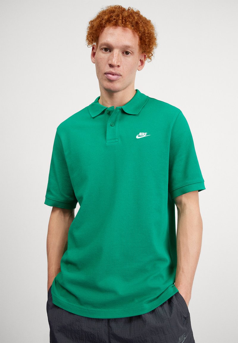 Zöld pamut póló, klasszikus gallérral, rövid ujjakkal és fehér Nike logóval a bal mellen. Sima tapintású.