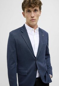 Tumesin blazeri tekstureeritud kangast, ühes nagu nööbianne sulgemine, krae, ja kaks esipocketit; valge särgi peale kihitatud.