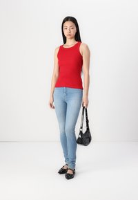 Top rojo sin mangas, jeans ajustados azules, zapatos planos negros con acentos de hardware y un pequeño bolso negro. Tejido suave y elástico.