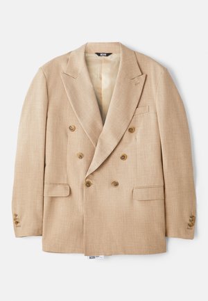 Beige dubbelknäppt kavaj med stora slag, två framfickor och bruna knappar, tillverkad av ett texturerat tyg.