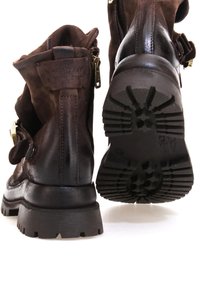 Stivali alla caviglia in pelle marrone con finitura scamosciata, cerniere laterali e cinturini decorativi. Suole spesse in gomma nera con un motivo scolpito.