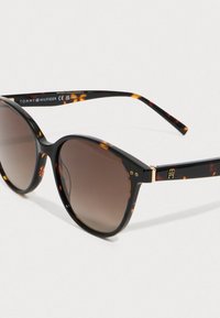 Gafas de sol de montura redonda de carey con lentes degradados en marrón y el logo dorado de Tommy Hilfiger en la patilla.