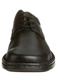 Zapato de vestir de piel negra con una textura suave, punta redonda y diseño de cinco ojetes para atar. Detalles cosidos a lo largo de la suela.