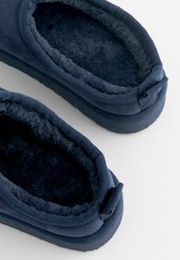 Mörkblå tofflor med mjukt, texturerat foder, rundad form och stickade kanter; med en enkel design och subtila klackdetaljer.
